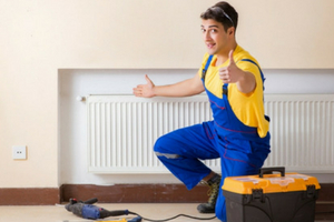 HVAC technician in blue overalls giving a thumbs up next to a heating radiator, with tools and a toolbox, emphasizing professional HVAC maintenance services.