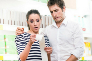 Couple looking shocked and concerned while examining a long receipt in a store, illustrating the potential financial impact of neglecting HVAC maintenance costs.