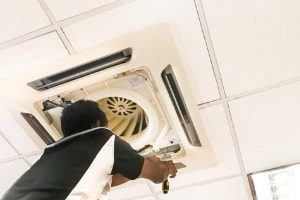 Technician servicing HVAC ceiling unit, emphasizing maintenance for improved system efficiency and reliability.