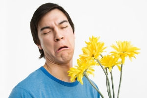 Man grimacing while holding a bouquet of yellow flowers, illustrating allergy discomfort related to indoor air quality.