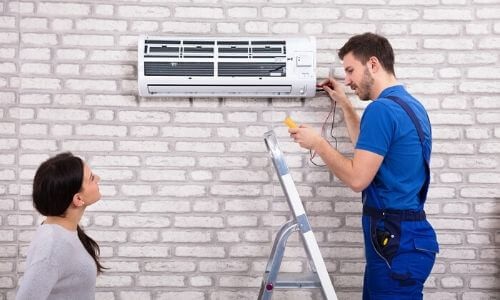 Male technician repairing air conditioning unit for homeowner near brick wall at Boutwell's Air Masters HVAC service.