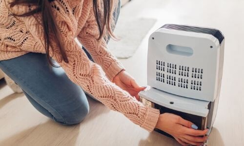 Woman kneeling beside a light blue air purifier, showcasing HVAC solutions for indoor air quality by Boutwell's Air Masters.
