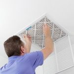 Person replacing a ceiling air filter, ensuring HVAC efficiency for summer maintenance tips by Boutwell's Air Masters.