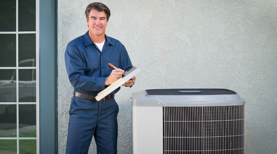Male technician in blue uniform working on air conditioning unit outdoors at Boutwell's Air Masters HVAC service.