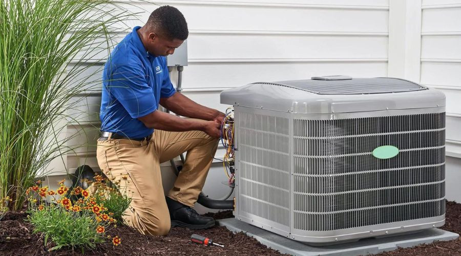 Technician repairing a gray air conditioning unit near orange flowers, highlighting Boutwell's Air Masters HVAC services.