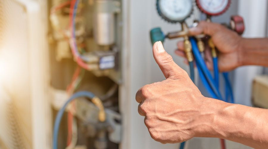 Technician giving a thumbs up while checking air conditioning system pressure gauges, emphasizing HVAC maintenance and efficiency.