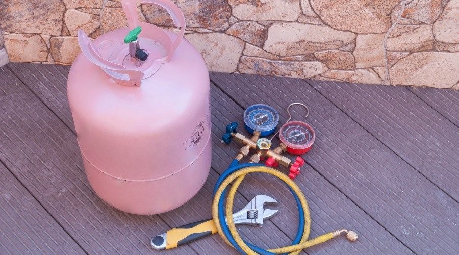Refrigerant tank and HVAC tools including pressure gauges, hoses, and a wrench, illustrating essential equipment for air conditioning maintenance and repair.
